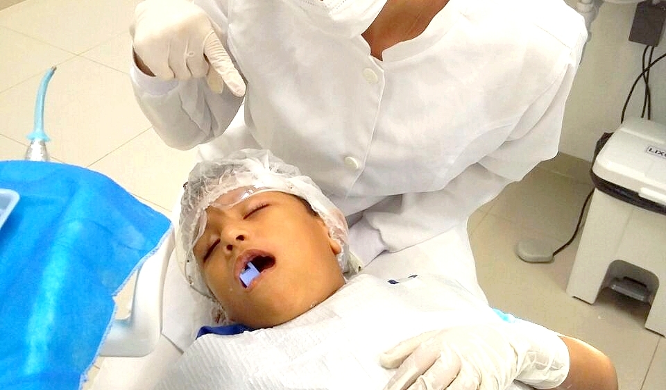 Criança dorme tranquila enquanto dentista faz obturação em seu dente na clínica da Uninorte
