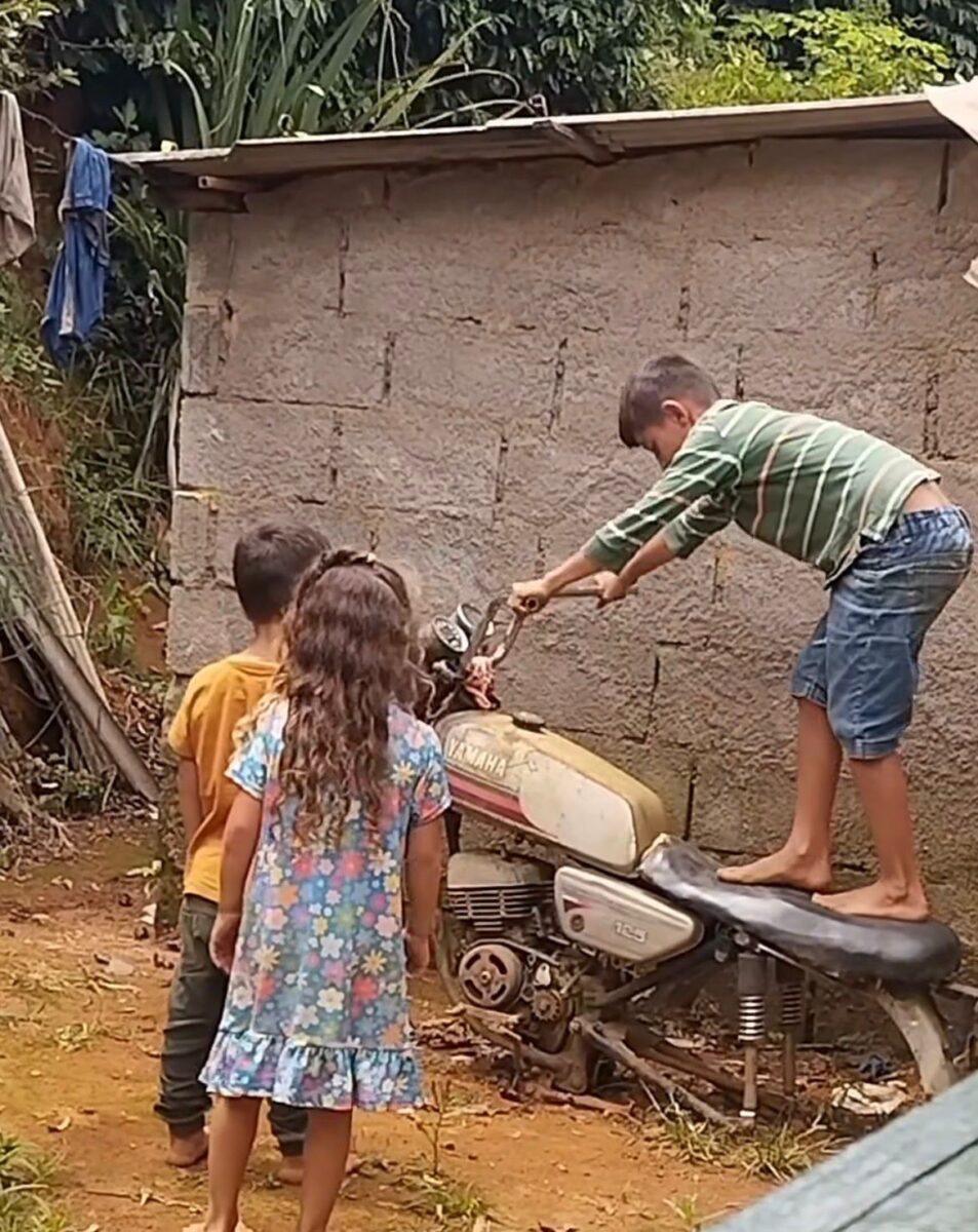 Vídeo mostra três crianças brincando com moto sem rodas em quintal e criatividade diverte internautas nas redes sociais.
