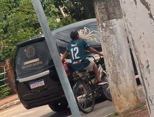 Pai acompanha cortejo de filho pedalando ao lado de carro funerário