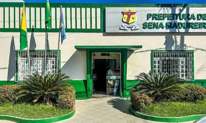 Imagem da Prefeitura de Sena Madureira com foco na fachada e pessoas ao redor.